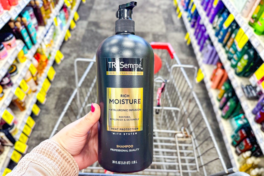 person holding a bottle of tresemme shampoo over a cart