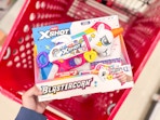 hand holding a xshot blastercorn toy blaster over a target cart