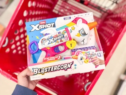 hand holding a xshot blastercorn toy blaster over a target cart