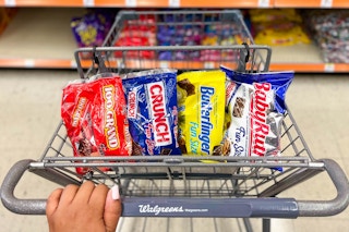 hand on shopping cart with a bag of Baby Ruth, Crunch, 100 Grand, and Butterfinger inside