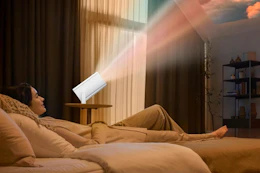 woman lying on bed next to mini projector