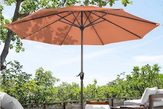 An orange 9-foot crank patio umbrella canopy and handle in a lush green setting