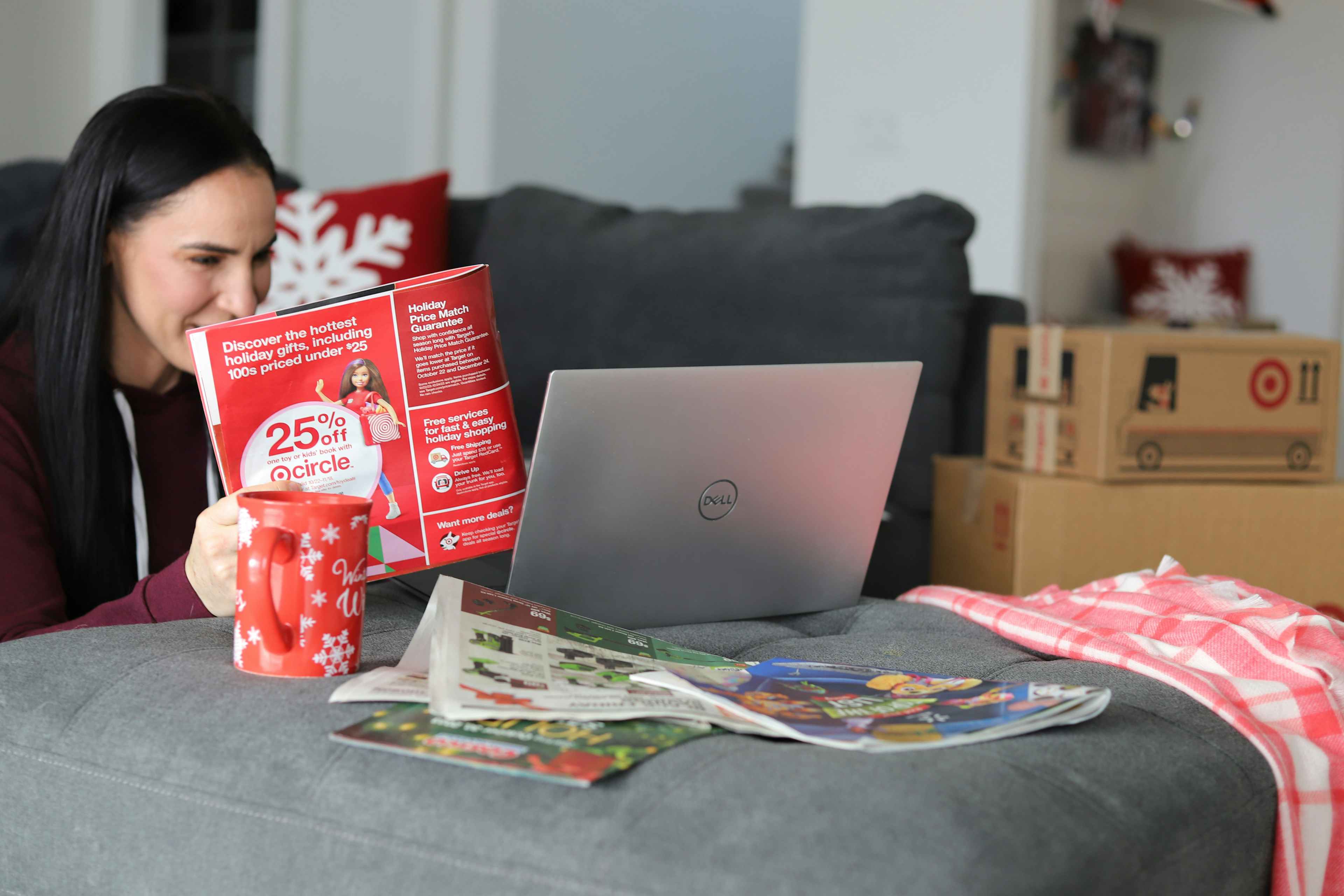 a woman looking at a target catalog while drinking coffee and sitting near the couch 