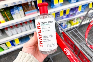person holding a bottle of thayers witch hazel toner over a cvs cart