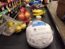 Food including a frozen turkey on a grocery store conveyer belt.