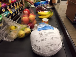 Food including a frozen turkey on a grocery store conveyer belt.