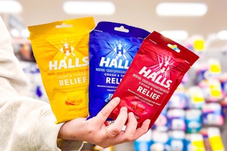 person holding 3 bags of halls cough drops