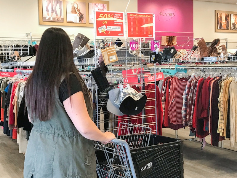 A woman pushing a shopping cart, looking at the clearance racks in Plato's Closet