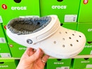 A person's hand holding a fuzzy Croc clog in a shoe store.