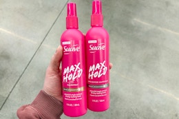 person holding 2 suave hair spray bottles