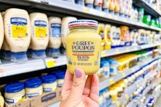 A hand holds up a jar of Grey Poupon mustard in the condiment aisle 