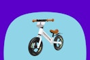 A white balance bike w. white frame, brown trim, and black 12-inch tires. It has a number 1 on a shield below the handlebars, and no pedals.