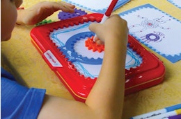 a kid drawing with a Spirograph Jr. at a table 