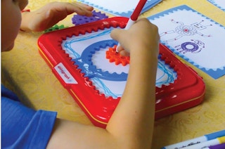 a kid drawing with a Spirograph Jr. at a table