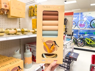 A 3 pack of Blogilatis resistance bands held out by hand in front of a store aisle.