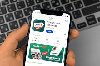 A person holding up a phone displaying the OfferUp app page in the IOS app store.