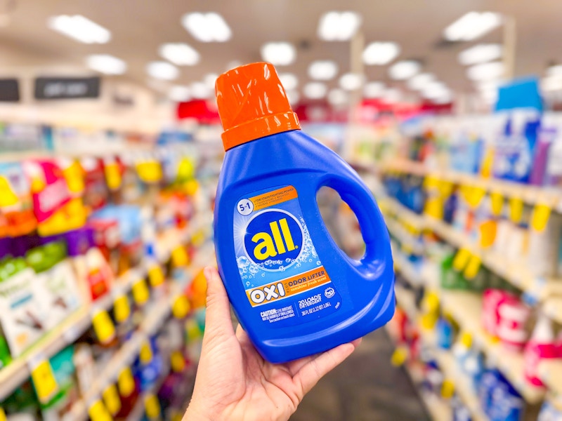 person holding up a bottle of all laundry detergent in an aisle