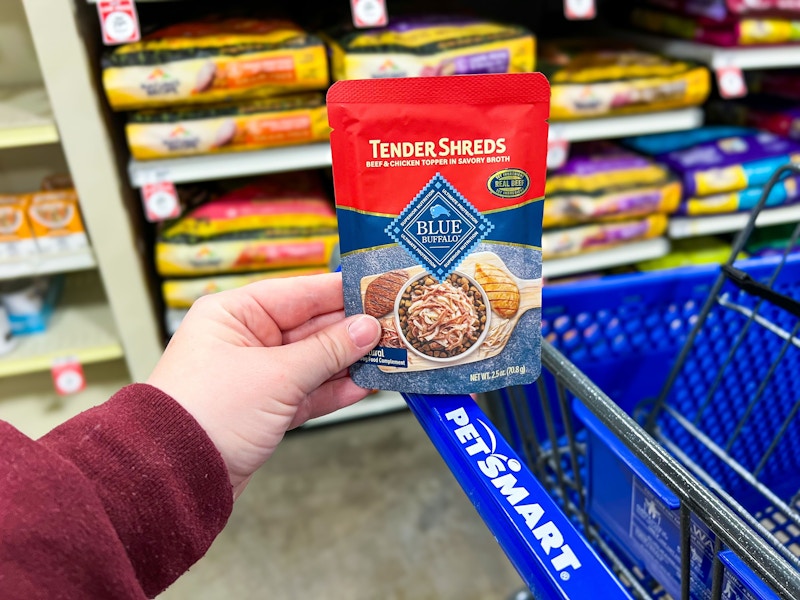 person holding a pack of blue buffalo tender shreds on a petsmart cart