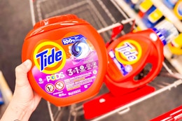 person holding a tub of tide pods over a cart with tide liquid detergent in it
