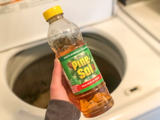 I bottle of Pine Sol in front of a top load washing machine.