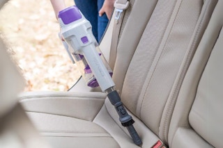 person using handheld vacuum on car seat
