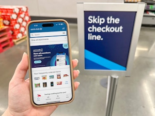 Someone holding up a phone displaying the Sam's Club app in front of the Sam's Club Scan and Go Fast Lane sign