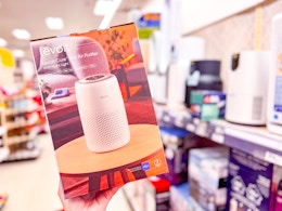 hand holding a levoit air purifier in front of a shelf