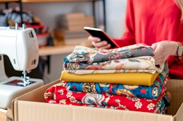 a woman in her sewing room looking at her phone and unboxing the fabric she ordered online