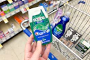 hand holding crest toothpaste over a shopping cart with other items