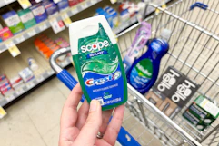 hand holding crest toothpaste over a shopping cart with other items