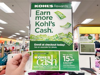 A person holding Kohl's cash near a Kohl's cash sign