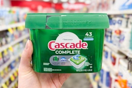 person holding a tub of cascade dishwasher pods in an aisle