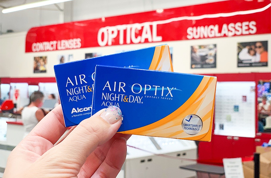 A person's hand holding up a box of contact lenses in front of costco optical department.