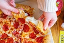 A person's hands taking a slice from a Hungry Howie's pizza.
