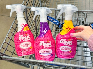 hand holding a bottle of the pink stuff spray with three in walmart cart