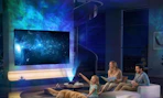 a galaxy light projecting on a wall and TV in room with a family