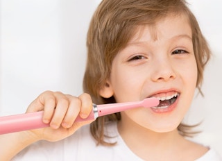 A child brushing his teeth with a pink electric toothbrush.