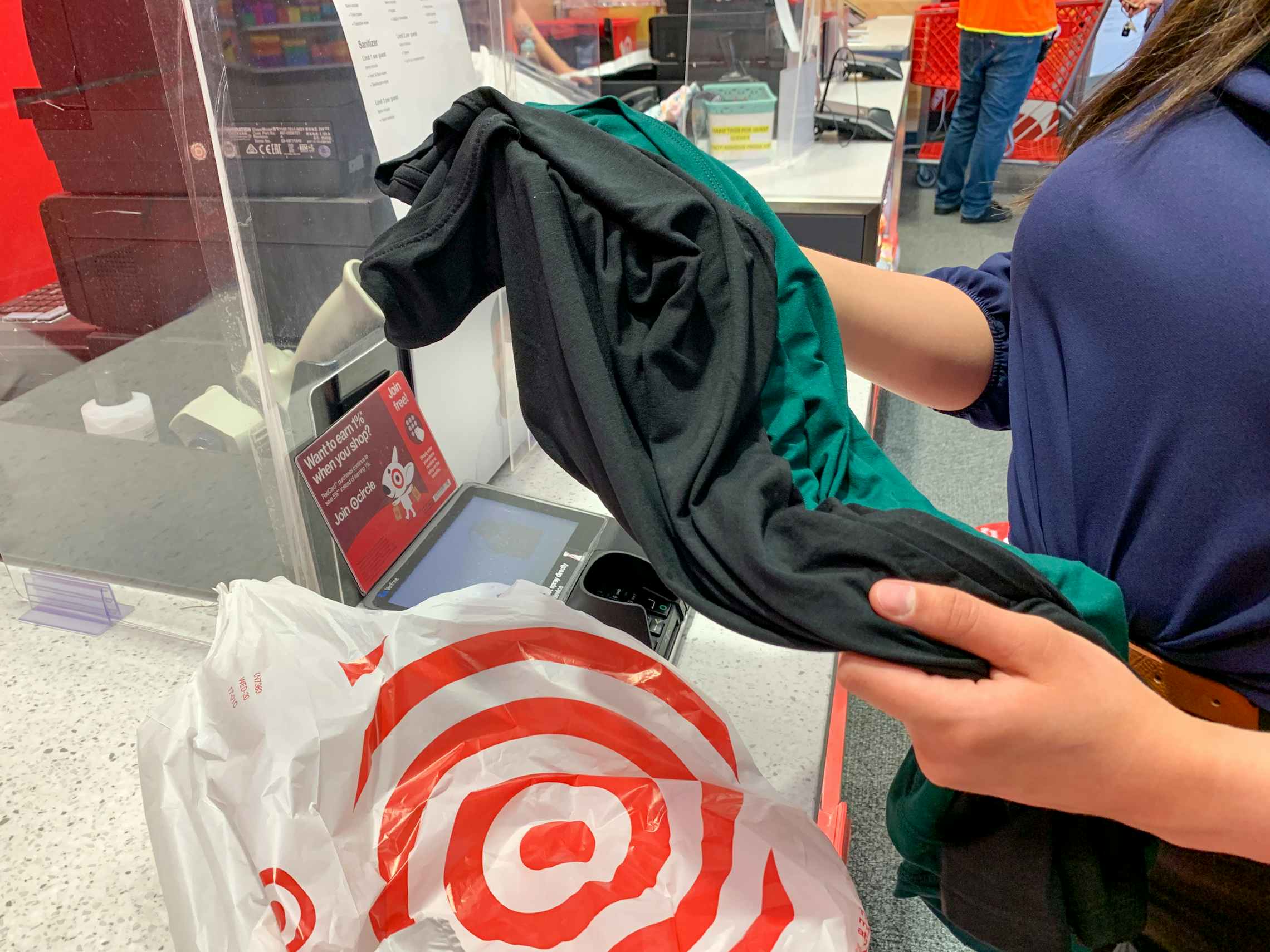 A woman holding two shirts at the Target return counter next to a Target grocery bag.