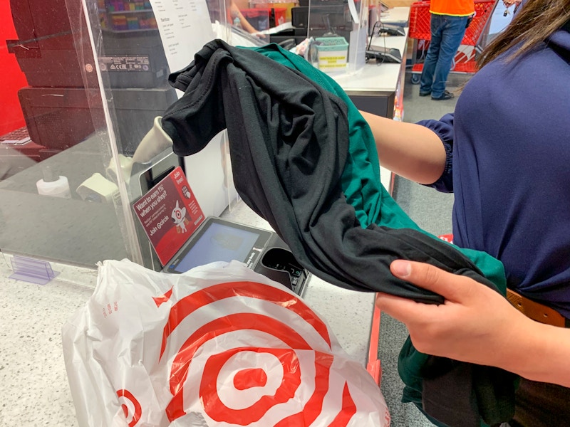 A woman holding two shirts at the Target return counter next to a Target grocery bag.