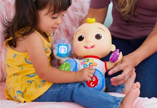 a child playing with the CoComelon doll on pink furniture