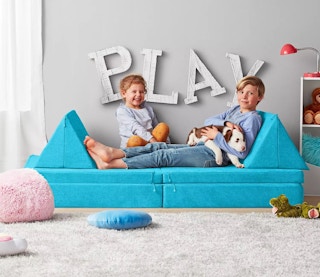 2 kids playing on a teal sofa that is repositionable for kids to play with