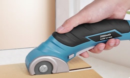 a hand using electric scissors on a piece of cardboard