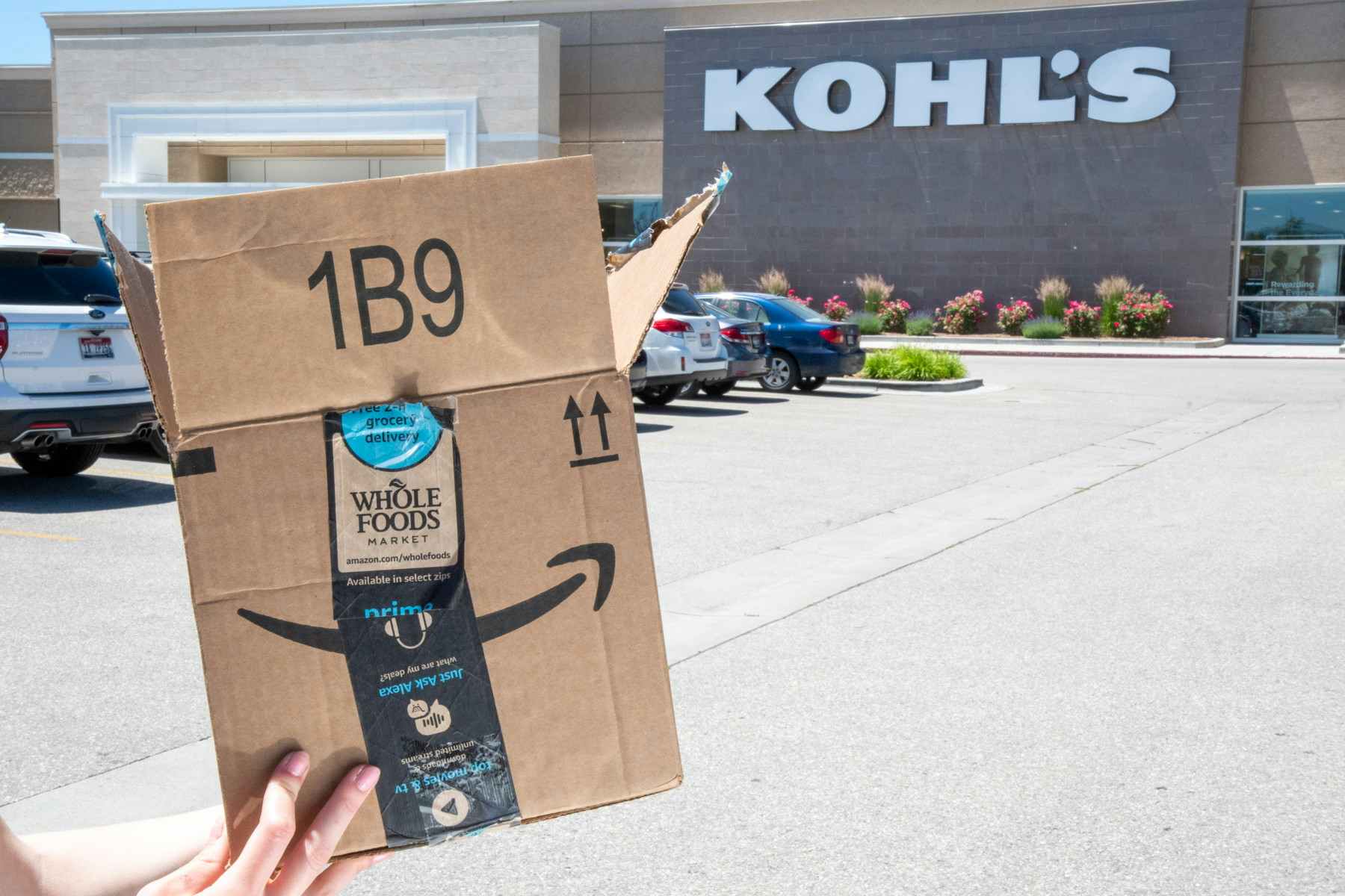 Someone is holding their Amazon purchase in front of a Kohl's storefront.