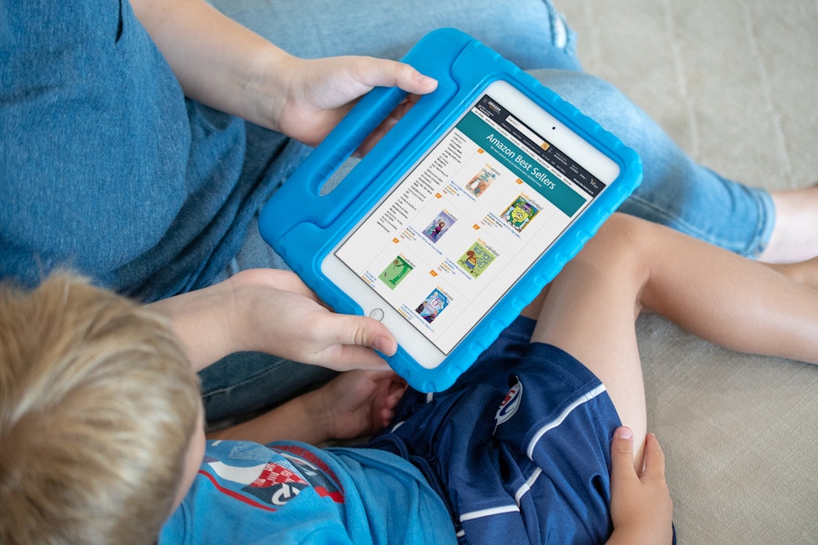 A small boy sitting with a woman on a sofa, looking at a tablet displaying free Amazon Kindle books for kids.