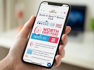 A person looking at a cellphone displaying the Build-A-Bear website page about their Bonus Club