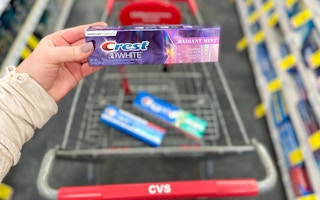 someone holding crest toothpaste next to cvs cart