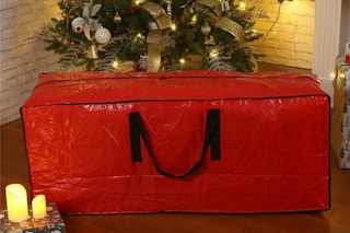 A red storage bag has a Christmas tree behind it.