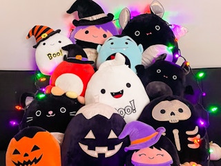 Halloween Squishmallows piled on a couch with string lights.