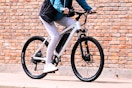 Adult riding a white 5th Wheel Electric bike outdoor by a brick building