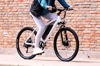 Adult riding a white 5th Wheel Electric bike outdoor by a brick building